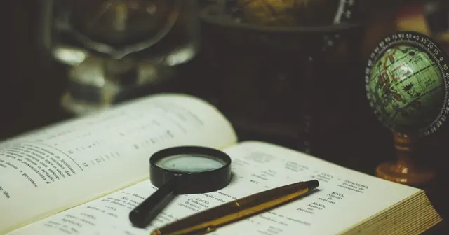 Lupa e caneta sobre um livro aberto