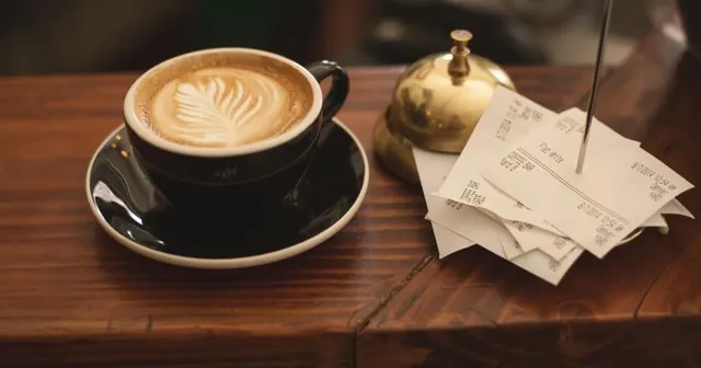 Cupons fiscais presos num espeto ao lado de uma xícara de café