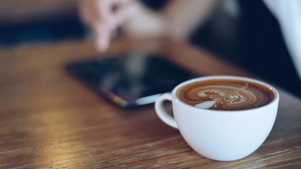 Celular e xícara de café sobre uma mesa de madeira