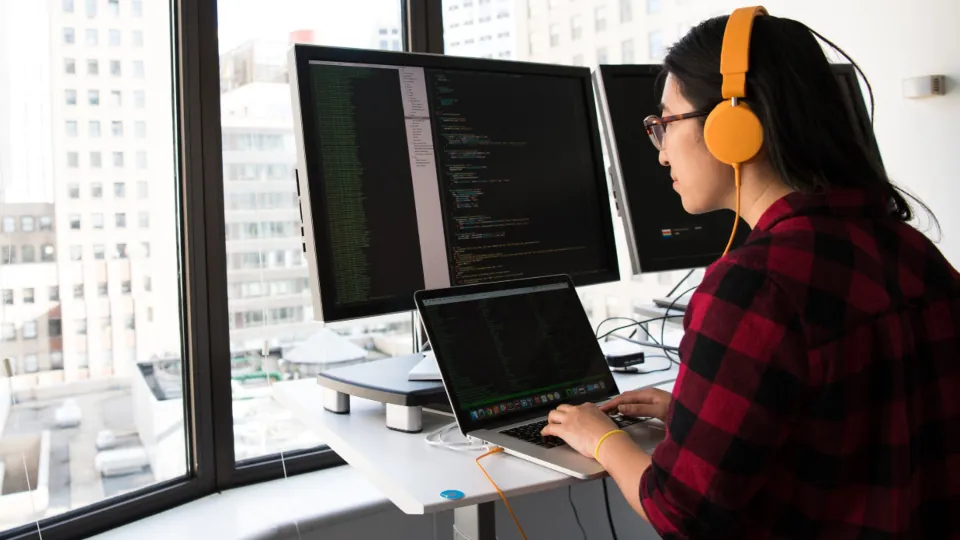 Programadora trabalhando diante de dois monitores
