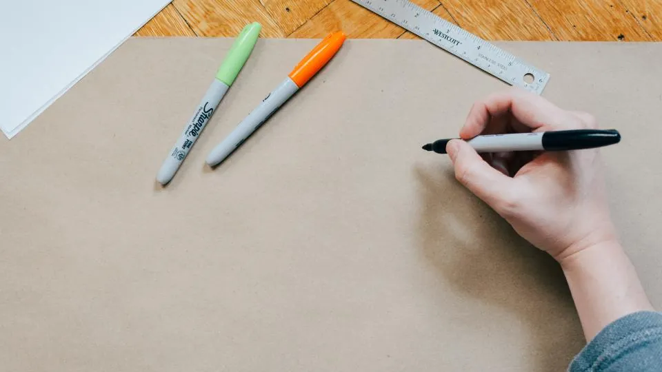 Pessoa desenhando sobre papel pardo com régua e canetas